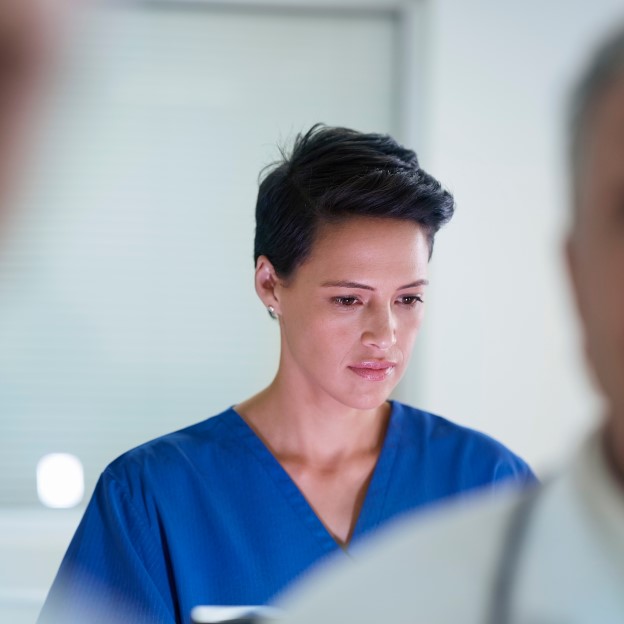 Female doctor wearing blue scrubs looking at computer with other doctors in the room
