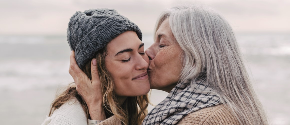 Two women, one older and one younger, embracing each other on a beach.