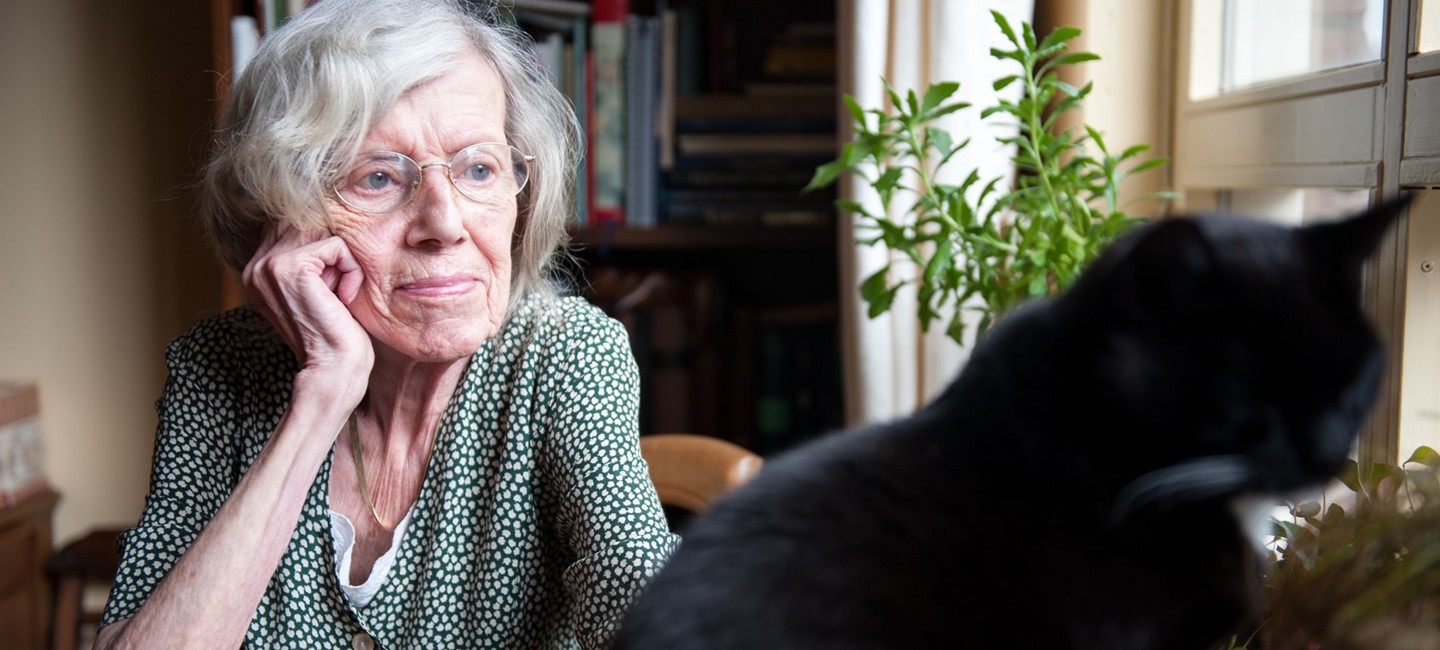 LADY OF ADVANCED YEARS, SITTING AT TABLE WITH CAT, LOOKING UNHAPPY