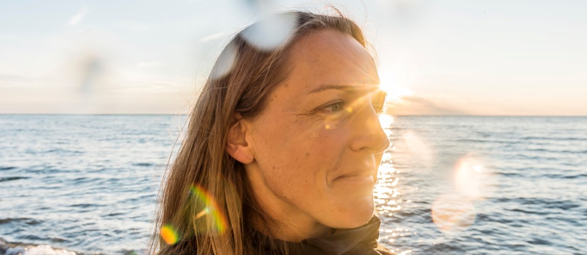 A stock photograph of a woman by the seaside with sunlight beaming behind her.